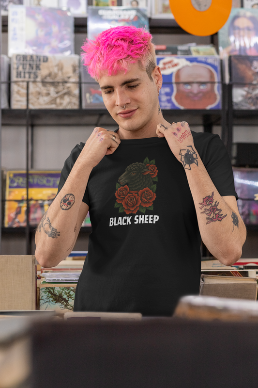A person with bright pink hair and tattoos stands in a record store, smiling and holding the collar of their Printify Black Sheep Tee. Vinyl records are displayed on shelves in the background.