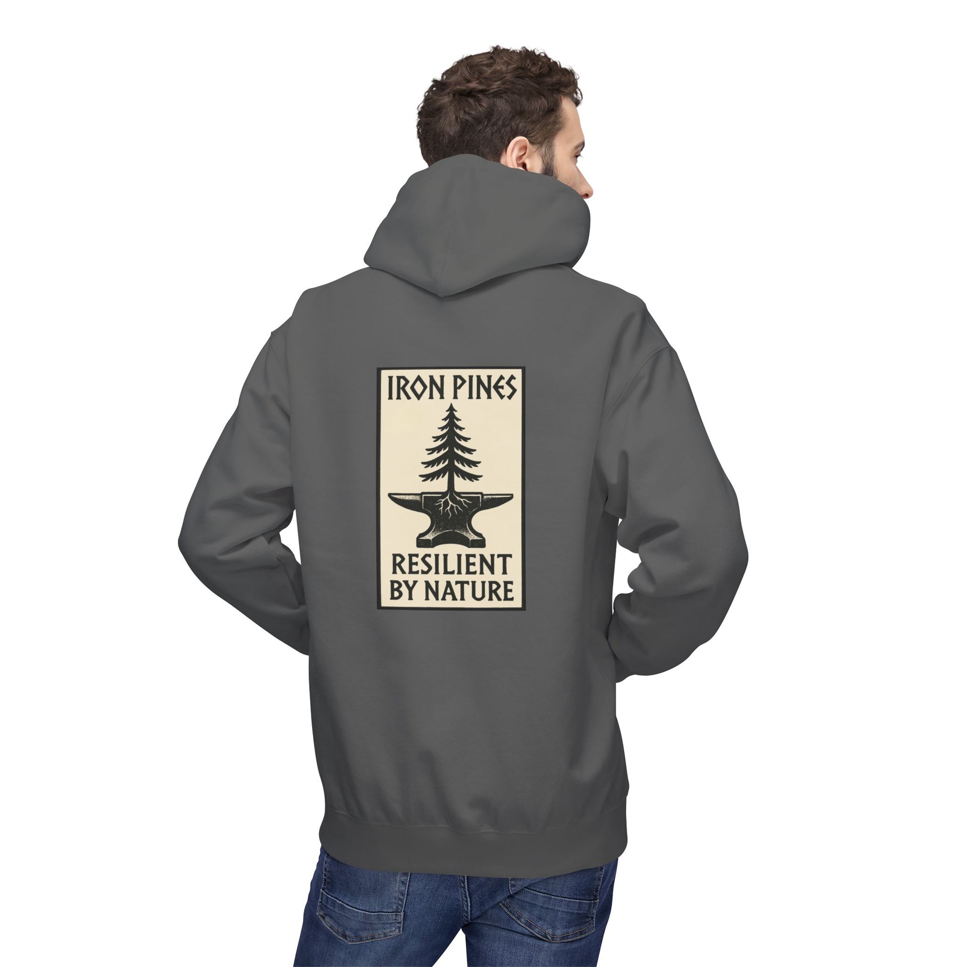 A man wears The Iron Pines Hoodie by Printify—a gray midweight fleece with a back graphic of a tree growing from an anvil and the words Iron Pines Resilient by Nature, ideal for fans of sustainable outdoor apparel.