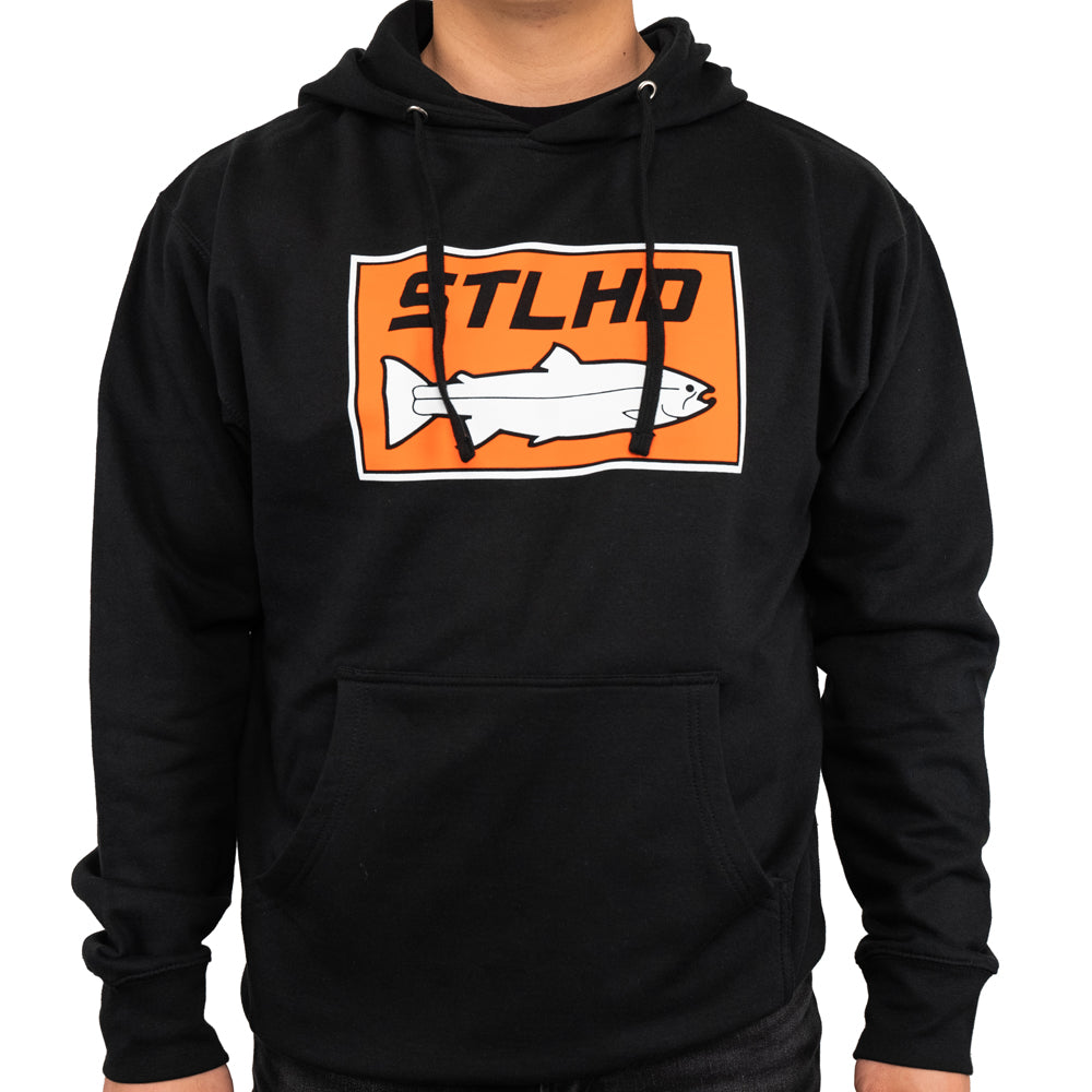 A man wears the STLHD GEAR Mens Standard Logo Black Standard Hoodie, a fleece-lined pullover with a front pocket and an orange and white STLHD logo featuring a fish outline on the chest.
