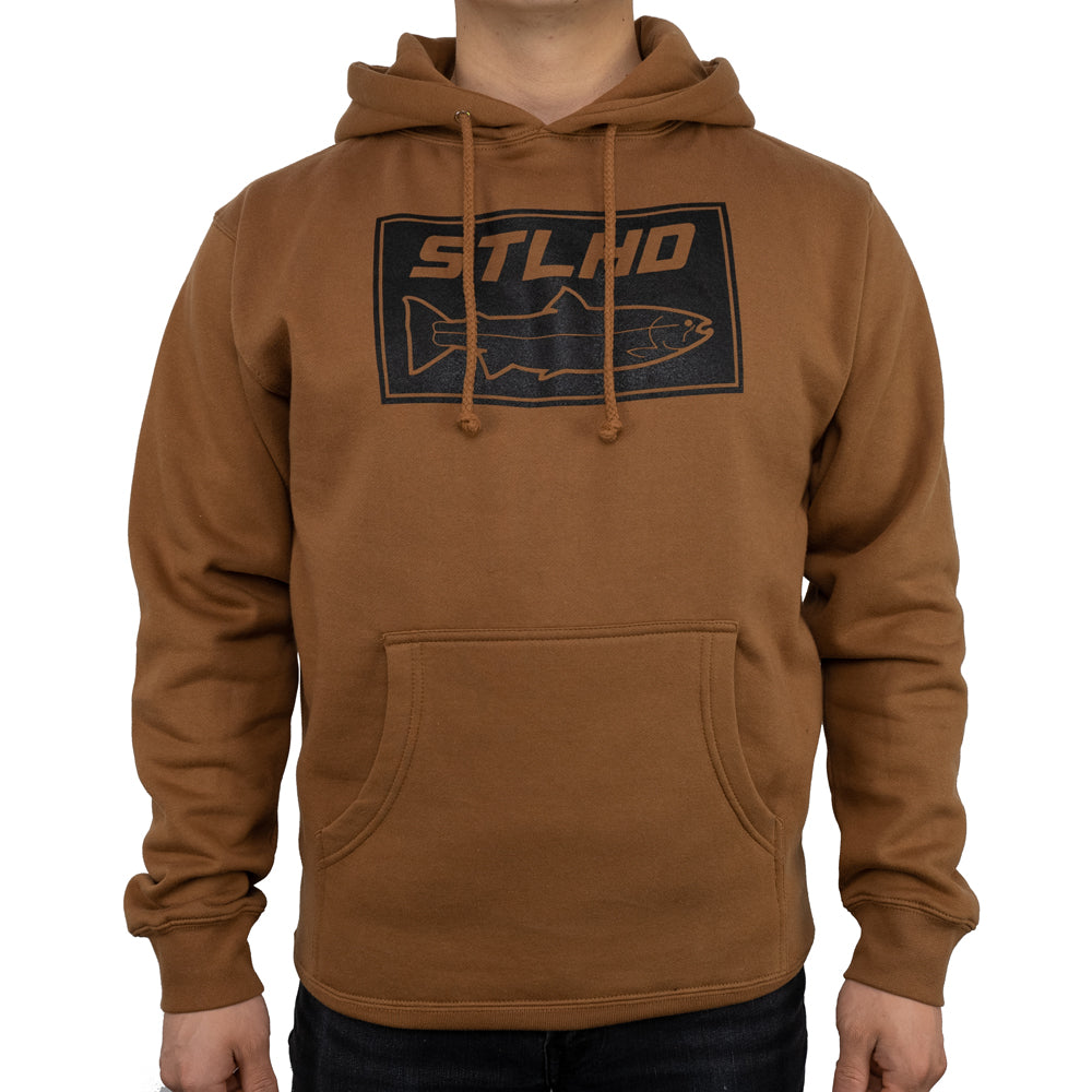 A person models the STLHD Mens Yuba River Saddle Brown Premium Hoodie by STLHD GEAR, featuring ultra-soft fleece lining, a front pocket, and a black rectangular graphic with STLHD above a fish outline. The head is not visible.