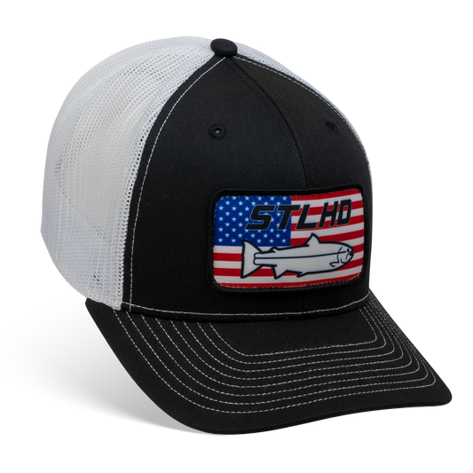 The STLHD GEAR Nation Black/White Trucker Snapback Hat features mesh back, adjustable snapback, an American flag patch, STLHD, and a wild steelhead fish outline on the front.