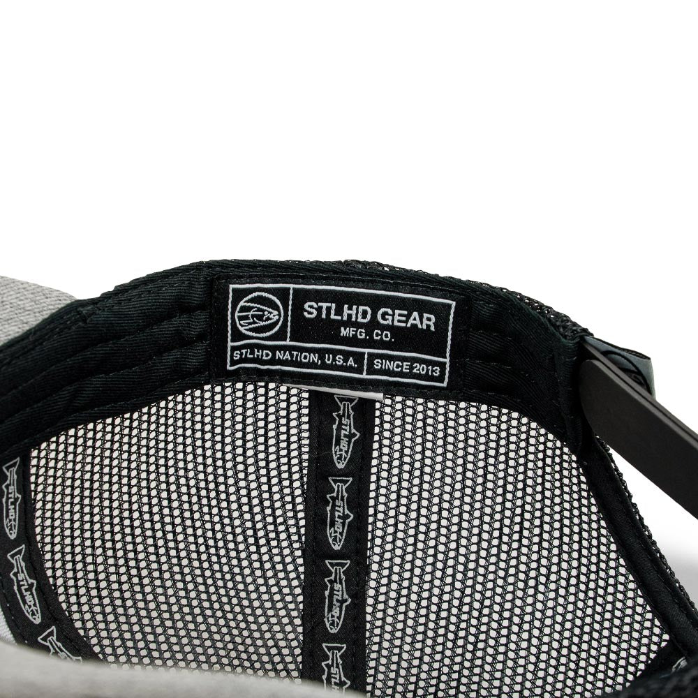 Close-up of the inside of the STLHD Chrome Edition Heather Grey/Black Trucker Snapback Hat by STLHD GEAR, showing a label with the logo, mesh lining, and adjustable snapback.