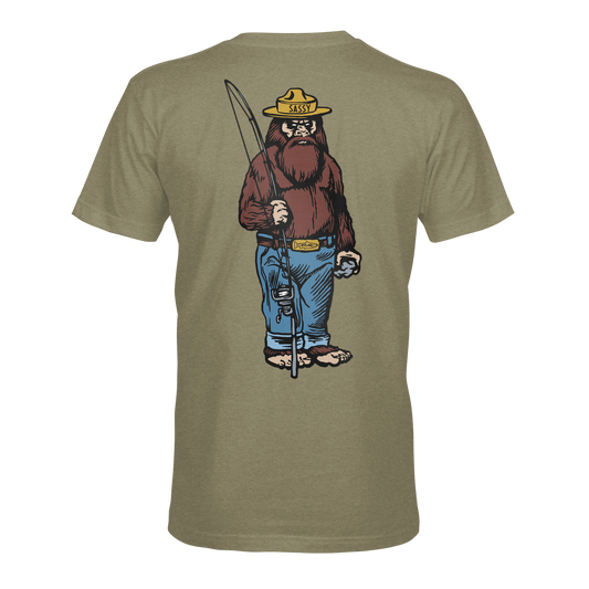 The STLHD Men’s Danger Ranger T-Shirt by STLHD GEAR features a cartoon Sasquatch in a yellow ranger hat and blue jeans with a fishing pole and tackle box, illustrated on the back of this olive green adventure shirt.