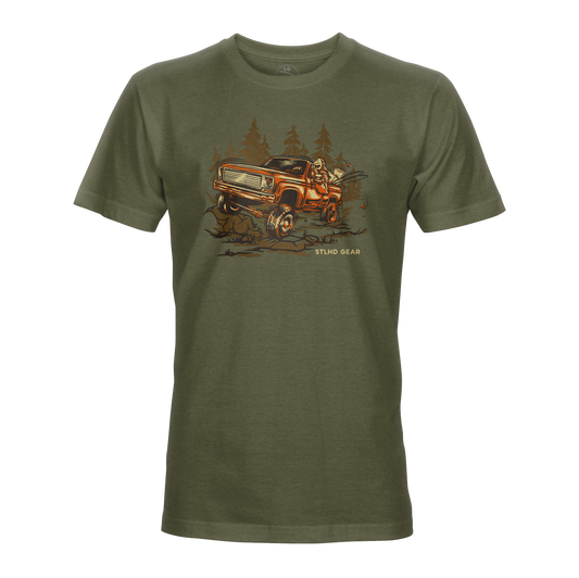 The STLHD GEAR Men’s 4x4 T-Shirt in olive features an orange off-road truck driving through a forest with Stud Gear text—a durable adventure tee made for outdoor enthusiasts.