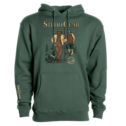 Green hoodie with graphic design of Bigfoot holding up a man with a fishing rod, with STLHD GEAR TEXT across the top', on a white background.