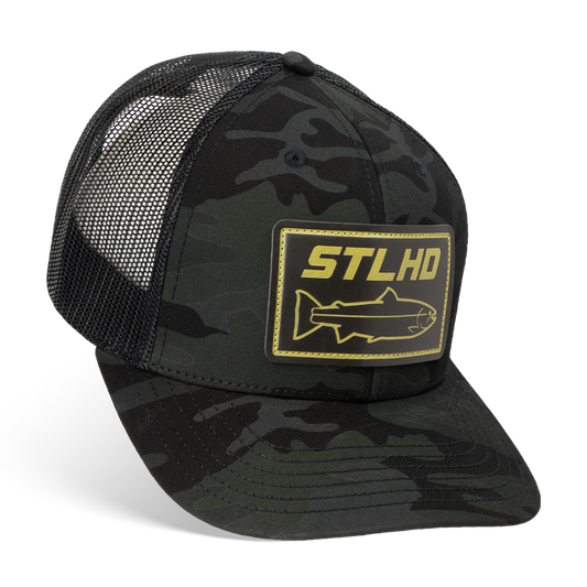 The STLHD GEAR Black Ops Multicam Snapback Trucker Hat features a black and dark camo design, a yellow STLHD fish patch on the front, breathable mesh back, and adjustable snapback for a comfortable fit.