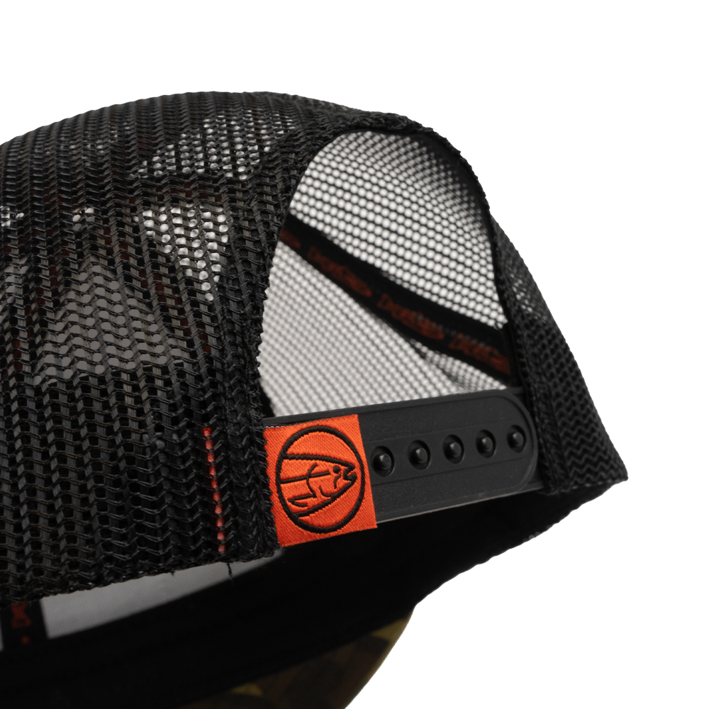 Close-up of the STLHD GEAR Camo Snapback Trucker Hat shows its black mesh back, adjustable snapback closure, and an orange fabric tag with a circular fish logo attached to the strap.