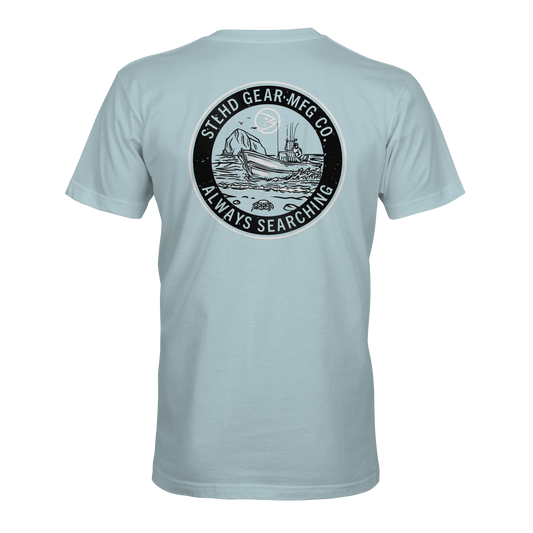 The STLHD Coastie T-Shirt by STLHD GEAR features a light blue design with a circular ship-at-sea graphic and STLHD GEAR MFG CO. ALWAYS SEARCHING text—ideal breathable comfort for any outdoorsmans collection.