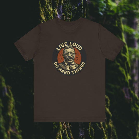 The Printify Live Loud, Do Hard Things Teddy Roosevelt Tee features a smiling Teddy in a circle, with LIVE LOUD above and DO HARD THINGS below, set against a blurred mossy forest background.