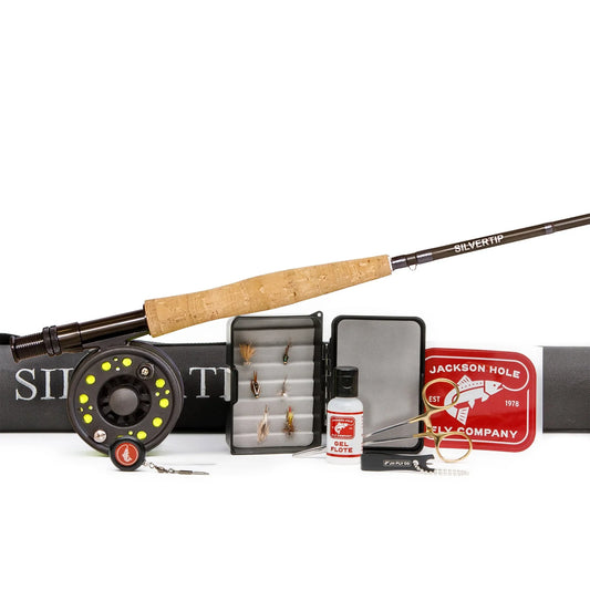 The Jackson Hole Fly Company Crystal Creek Fly Fishing Combo Kit – 90 5WT Beginner Set includes a fly rod, reel, case, assorted flies in a box, essential tools, floatant, and a red company tin—all arranged on a white background.