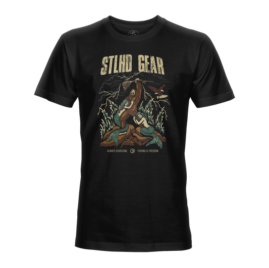 The STLHD King of the Mountain T-Shirt by STLHD GEAR features vintage Bigfoot and mermaid art with lightning and trees, plus “Always Searching” and “Fishing for Freedom” phrases. A breathable tee perfect for outdoor adventure seekers.