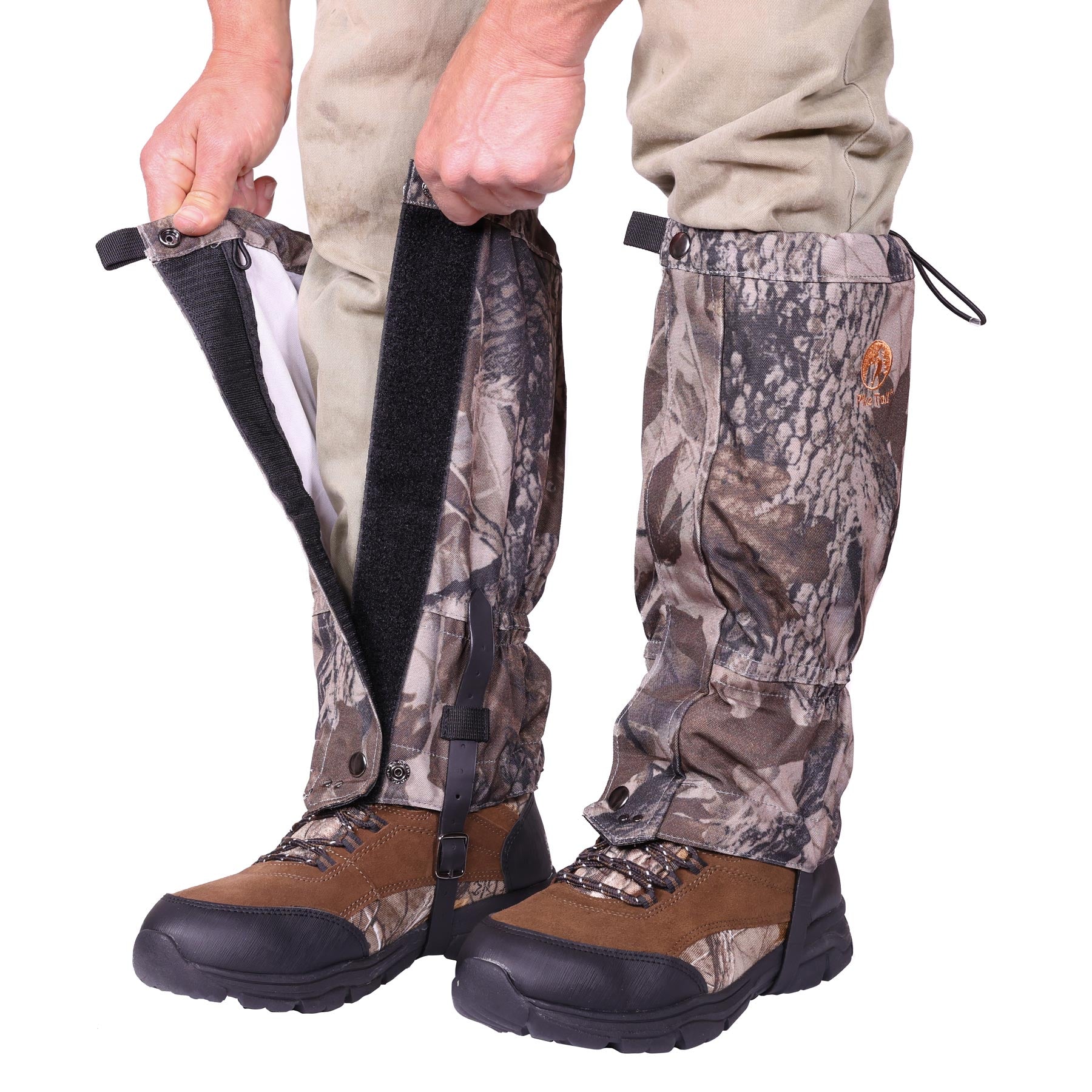 A person is fastening Pike Trail All-Season Waterproof Leg Gaiters with a camouflage pattern and Velcro closure over tan pants and brown hiking boots.