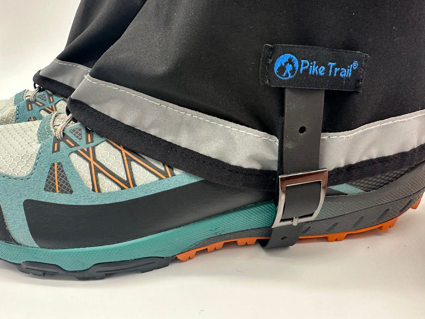 A close-up shows a hiking shoe with the Pike Trail Mid-Length Gaiter – Small/Medium Adjustable Fit in blue and black. These waterproof gaiters feature a reflective strip, the Pike Trail logo, and secure with a metal buckle around the shoe.