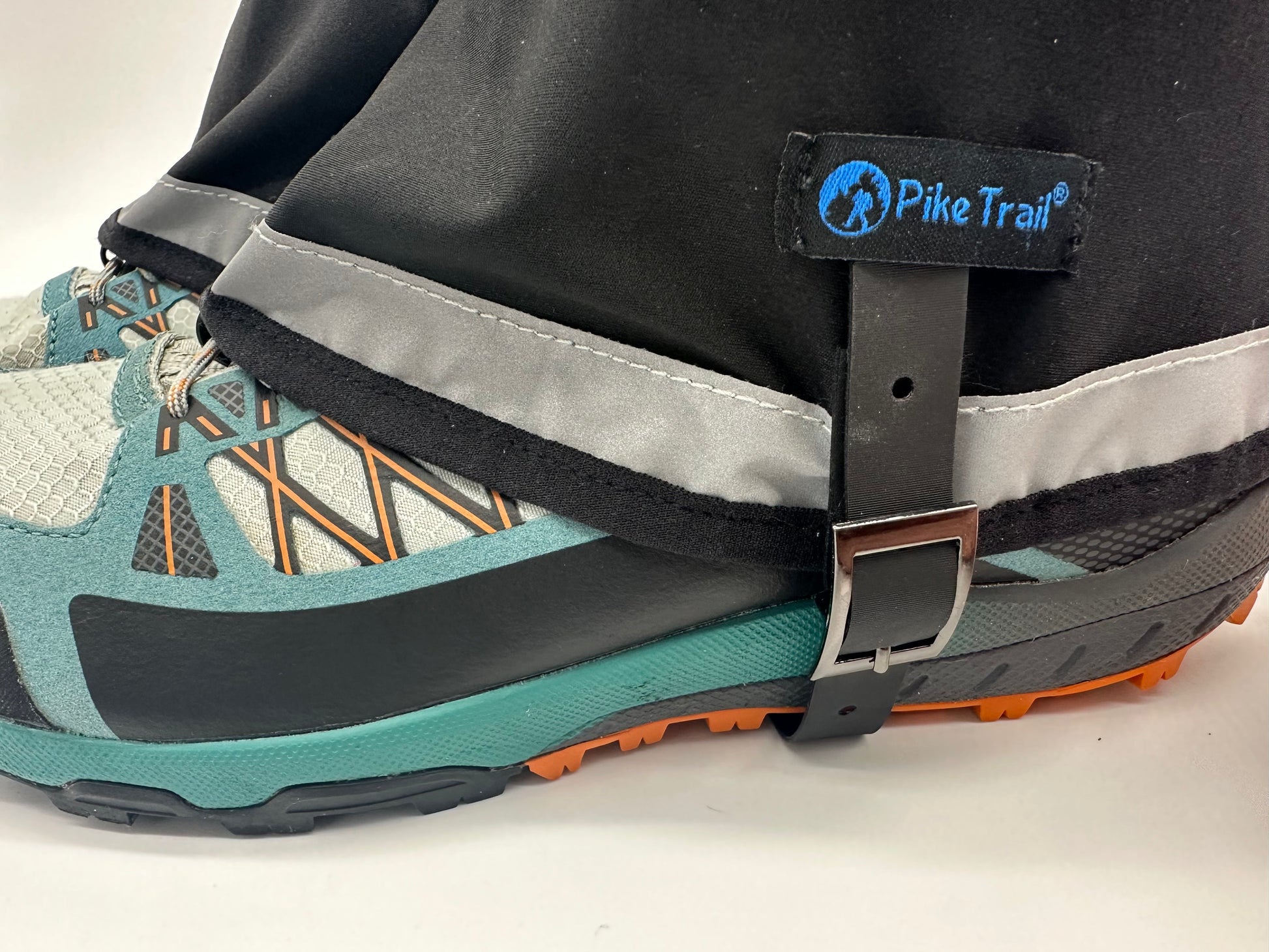 A close-up shows a hiking shoe with the Pike Trail Mid-Length Gaiter – Small/Medium Adjustable Fit in blue and black. These waterproof gaiters feature a reflective strip, the Pike Trail logo, and secure with a metal buckle around the shoe.