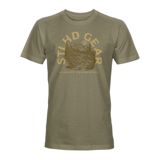 The STLHD Mountain View T-Shirt by STLHD GEAR is an olive green, breathable tee with a gold mountain, tree, and sun graphic. “STLHD GEAR” is above and “ALWAYS SEARCHING” below—ideal for outdoor adventure seekers.