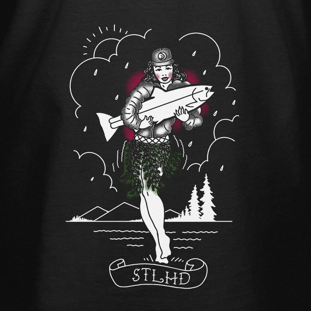 Black t-shirt with a graphic design of hula dancer holding a fish and trees with STLHD in script bellow, set against a dark background.