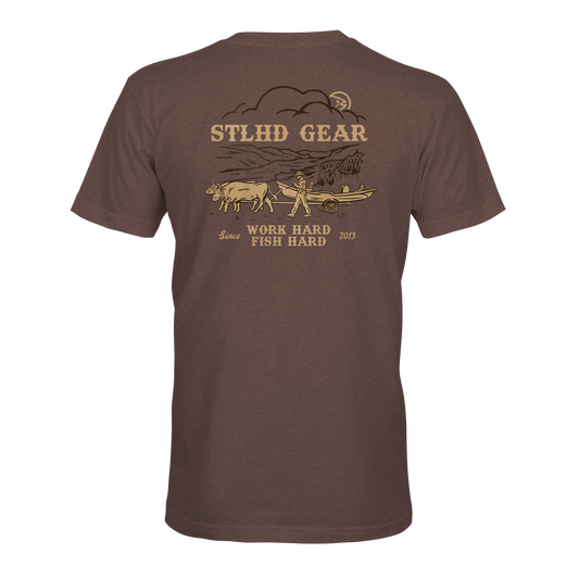 The STLHD Oregon Trail T-Shirt from STLHD GEAR features a man pulling a boat with an ox, yellow and beige graphics, WORK HARD FISH HARD slogan, and breathable comfort—perfect for every adventure since 2013.