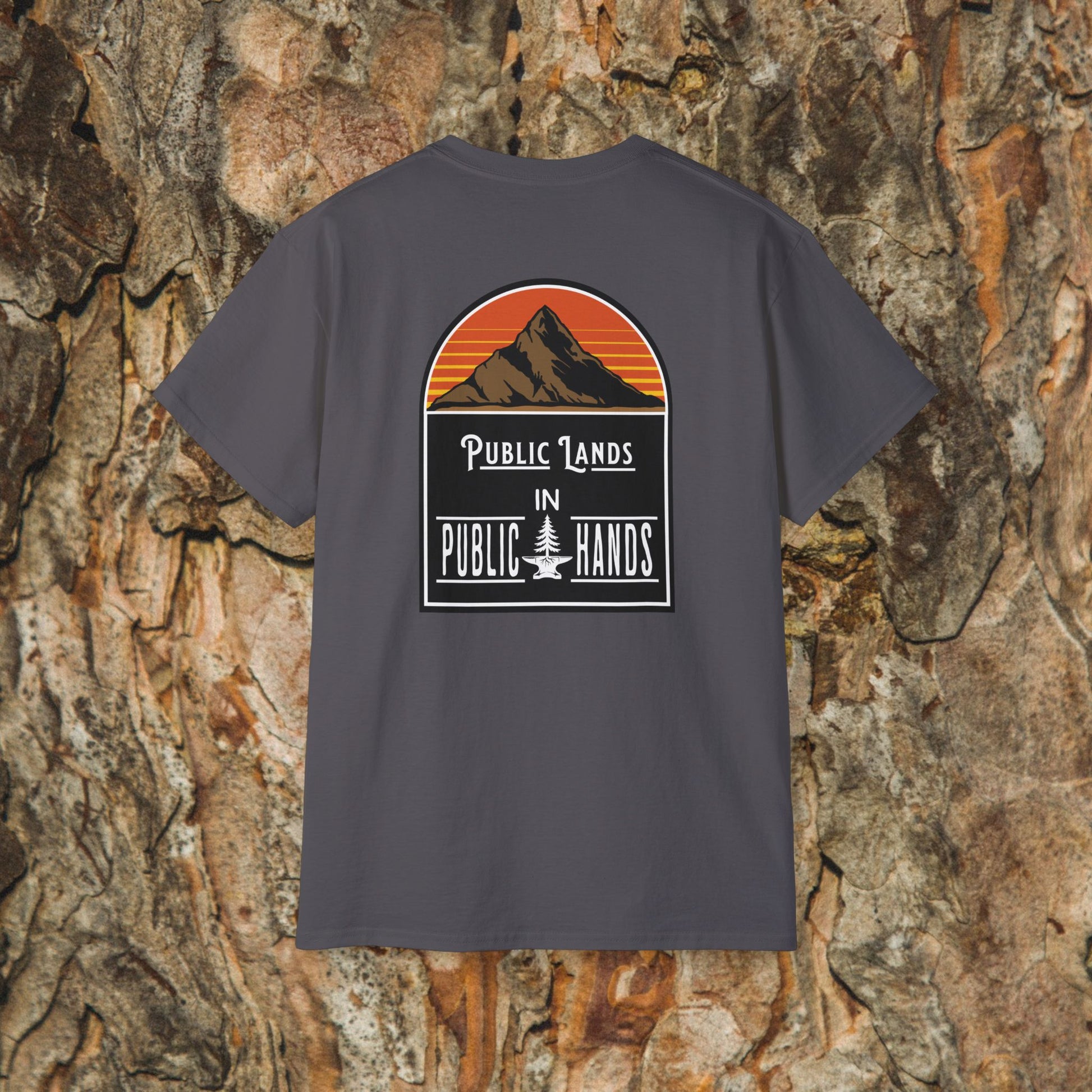The Iron Pines Public Lands in Public Hands Tee features a sunset mountain and pine graphic with the slogan “Public Lands in Public Hands,” made from ethically sourced cotton, shown against textured tree bark.