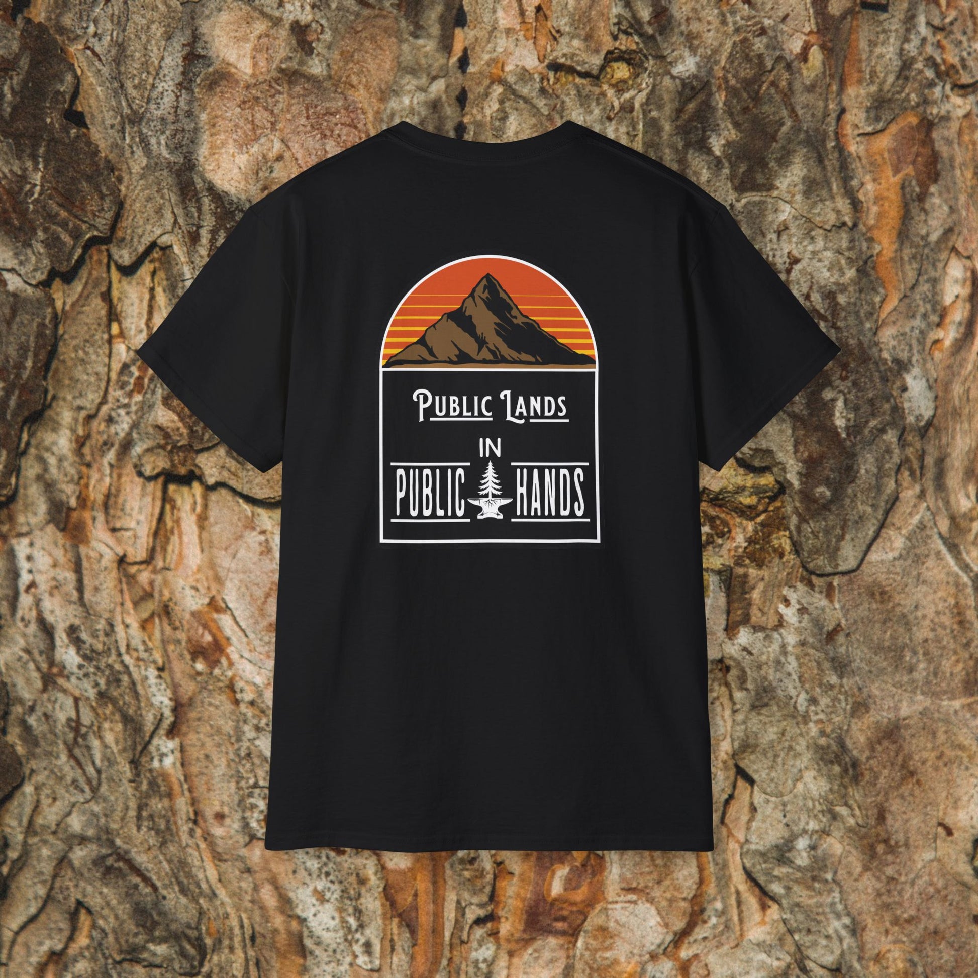 The Iron Pines Public Lands in Public Hands Tee is a black hiking shirt with a mountain and sunset graphic above the slogan, crafted from ethically sourced cotton and shown against textured tree bark.