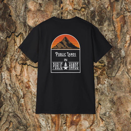 The Iron Pines Public Lands in Public Hands Tee is a black hiking shirt with a mountain and sunset graphic above the slogan, crafted from ethically sourced cotton and shown against textured tree bark.