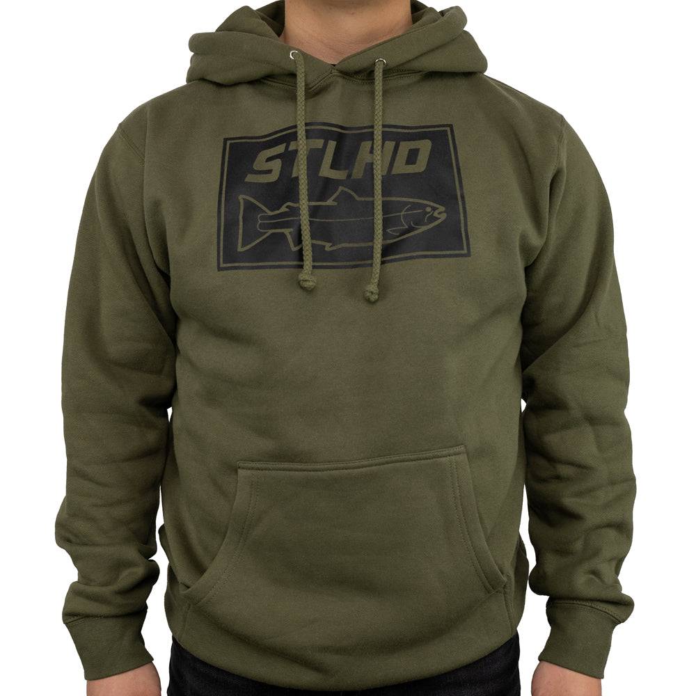 A person wearing the STLHD Mens Tidewater Army Green Premium Hoodie by STLHD GEAR, a fleece-lined hoodie with a front pocket and a rectangular chest logo featuring STLHD text and an outlined fish.