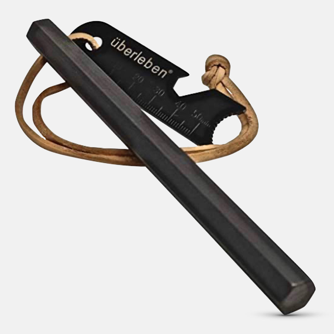 The Überleben Hexå Original Fire Starter features a black ferro rod, brown leather cord, and a metal striker with measurement lines—perfect for outdoor fire starting.