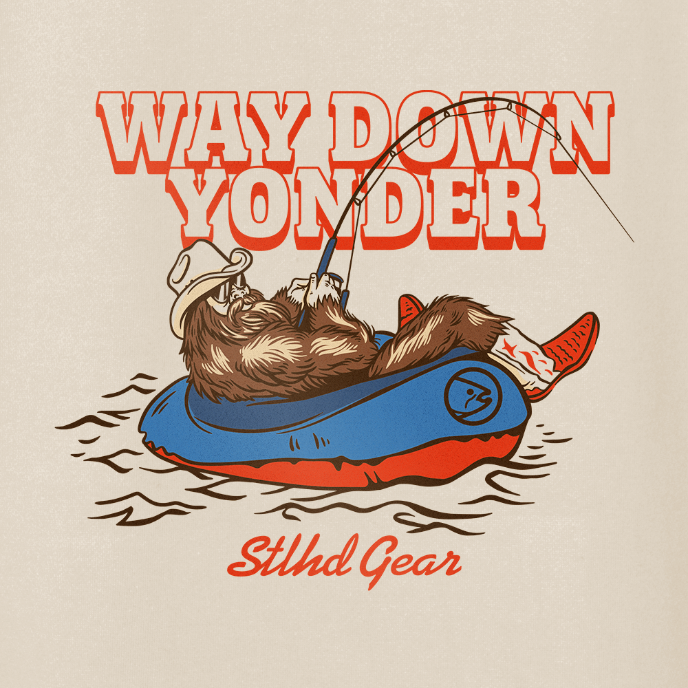 an image featuring  Way down yonder STLHD GEAR text and an image of bigfoot with cowboy boots and hat fishing from a raft in a body of water. on a beige background.