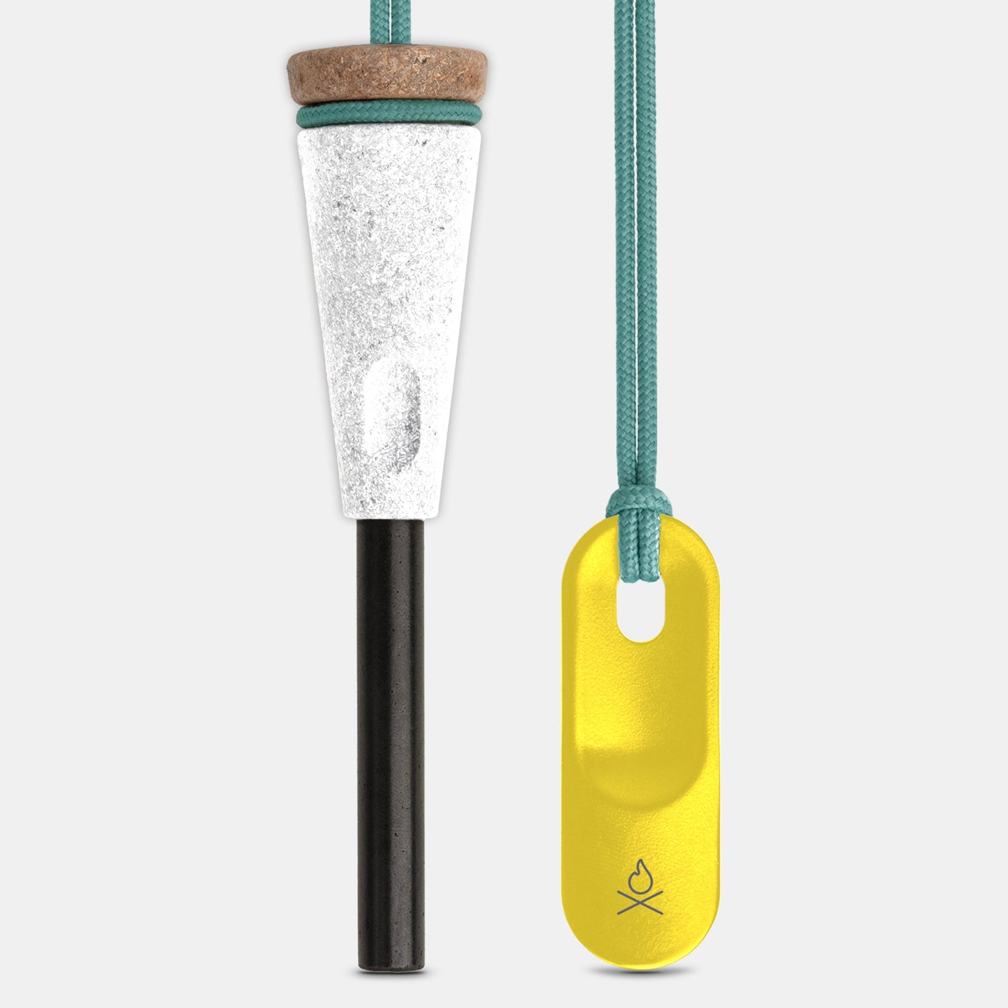 The Überleben Zünden PRO Fire Starter by Überleben, with a wood-composite handle, white and black ferro rod, cork top, and teal cord, sits beside a yellow metal tag with teal cord and a heart logo at the bottom.