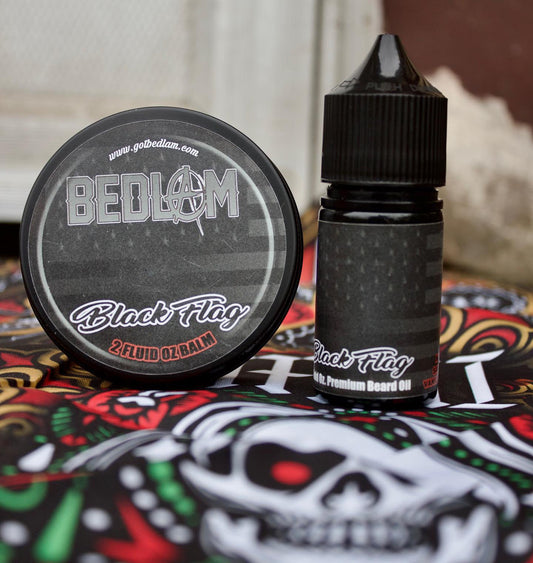 A tin of Bedlam Beard Companys BLACK FLAG Beard Balm and a bottle of BLACK FLAG Beard Oil rest on skull-patterned fabric, featuring black labels with white and red text and a bold, masculine scent.