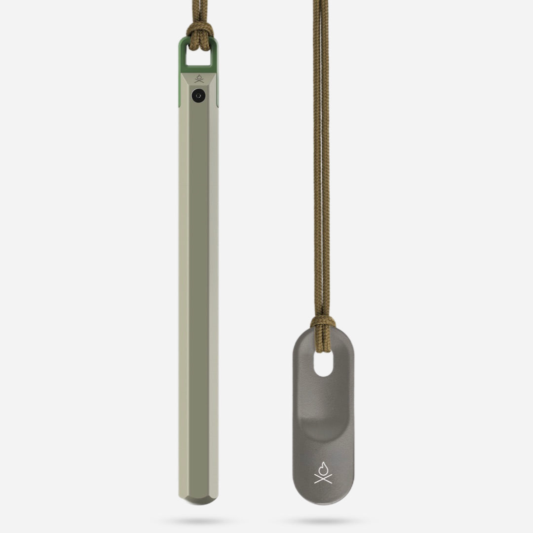 Two slender metal tools on cords—one green, one gray—each with a small Überleben logo; these are Überleben Hexå PRO ferro rod fire starters, minimalist survival gear shown against a plain white background.