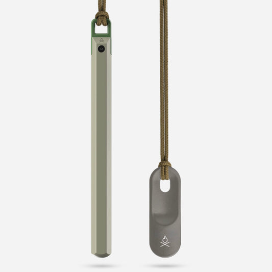 Two slender metal tools on cords—one green, one gray—each with a small Überleben logo; these are Überleben Hexå PRO ferro rod fire starters, minimalist survival gear shown against a plain white background.