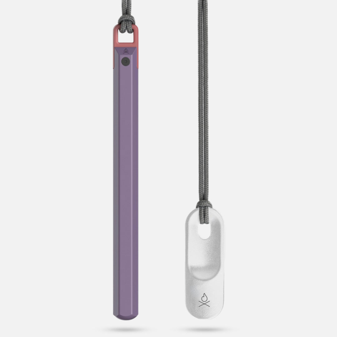 Two pendant-style inhalers on cords: one is a long, slim, purple and pink device with a button; the other resembles the Überleben Hexå PRO by Überleben—a compact fire starter with a small white oval holder featuring an opening and logo.
