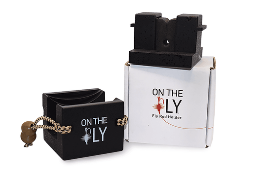 Two black On The Fly – Universal Fly Rod & Reel Holders by Jackson Hole Fly Company are shown—one on a string, one on a branded box with a fly graphic—ideal for organizing fishing gear or mounting your rod and reel to your vehicle.