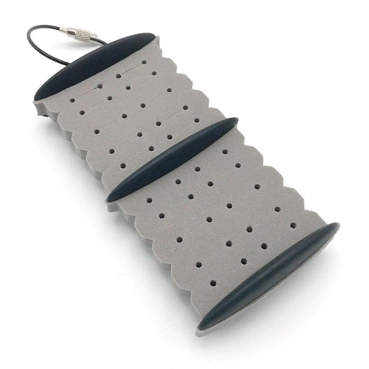 The Smith Creek Rig Keeper by Jackson Hole Fly Company is a gray foam rig holder with scalloped edges, black plastic ends, and a metal cable loop for easy carrying—an ideal fly fishing storage solution shown on a white background.