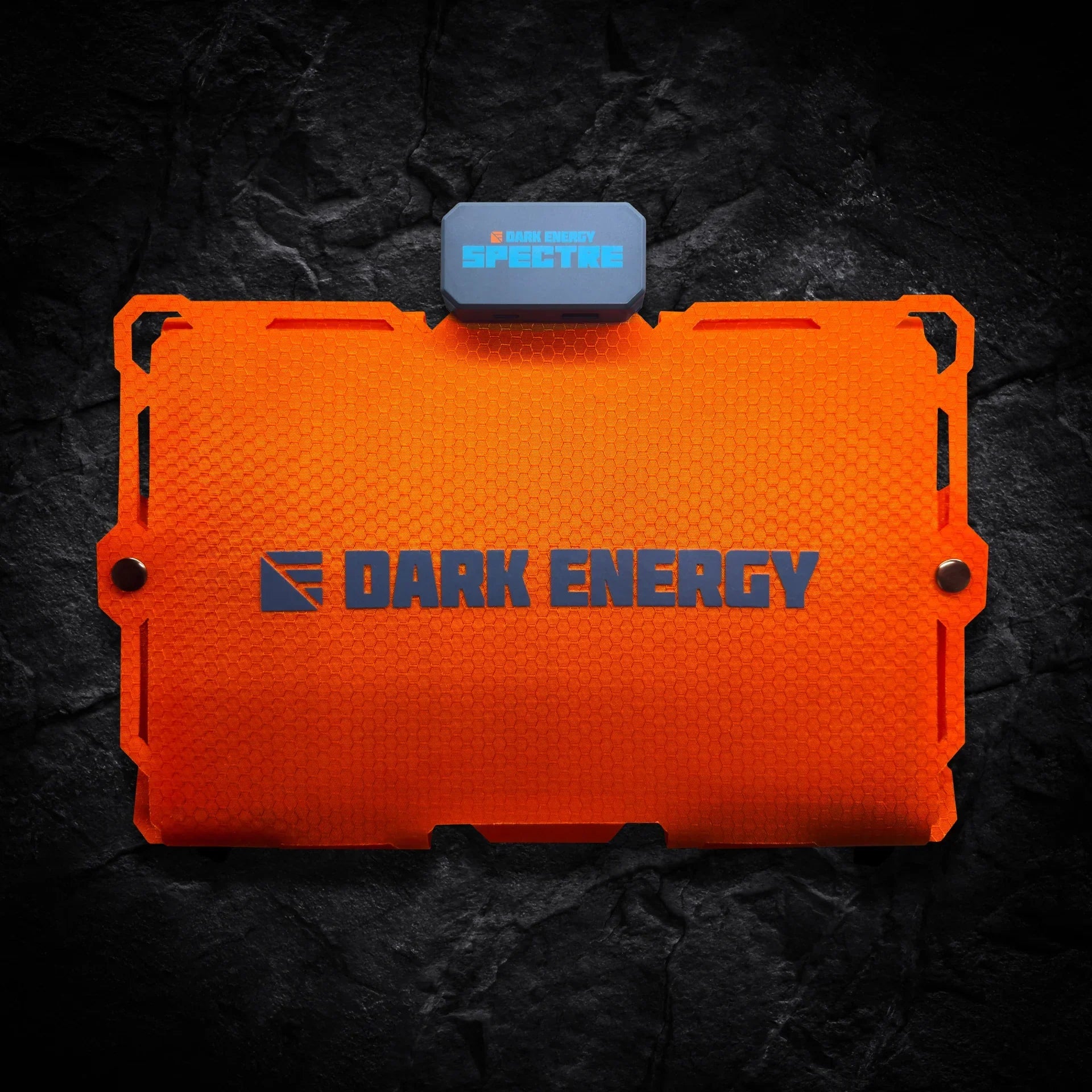 An orange rectangular Entropy Survival Off Grid Survival Power Bundle with a textured finish, plus a small attached blue-gray SPECTRE unit, shown on a dark rocky background.