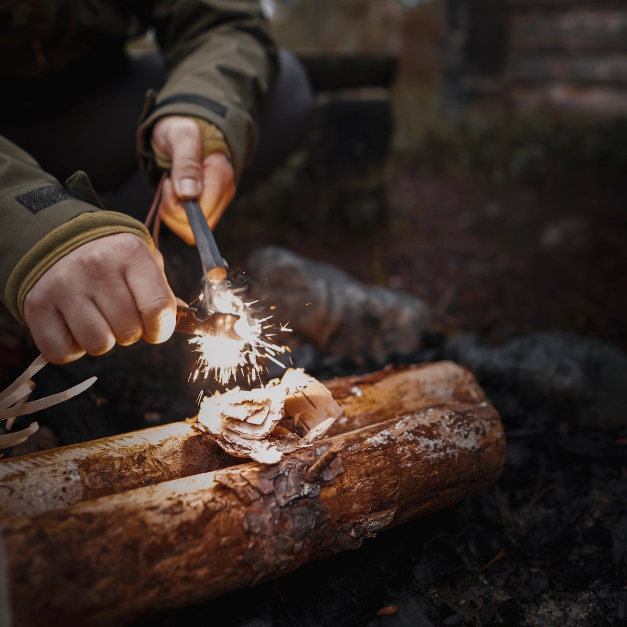 Using the Überleben Hexå Original Fire Starter, someone creates sparks over bark and kindling on a log, getting ready to start a campfire outdoors.