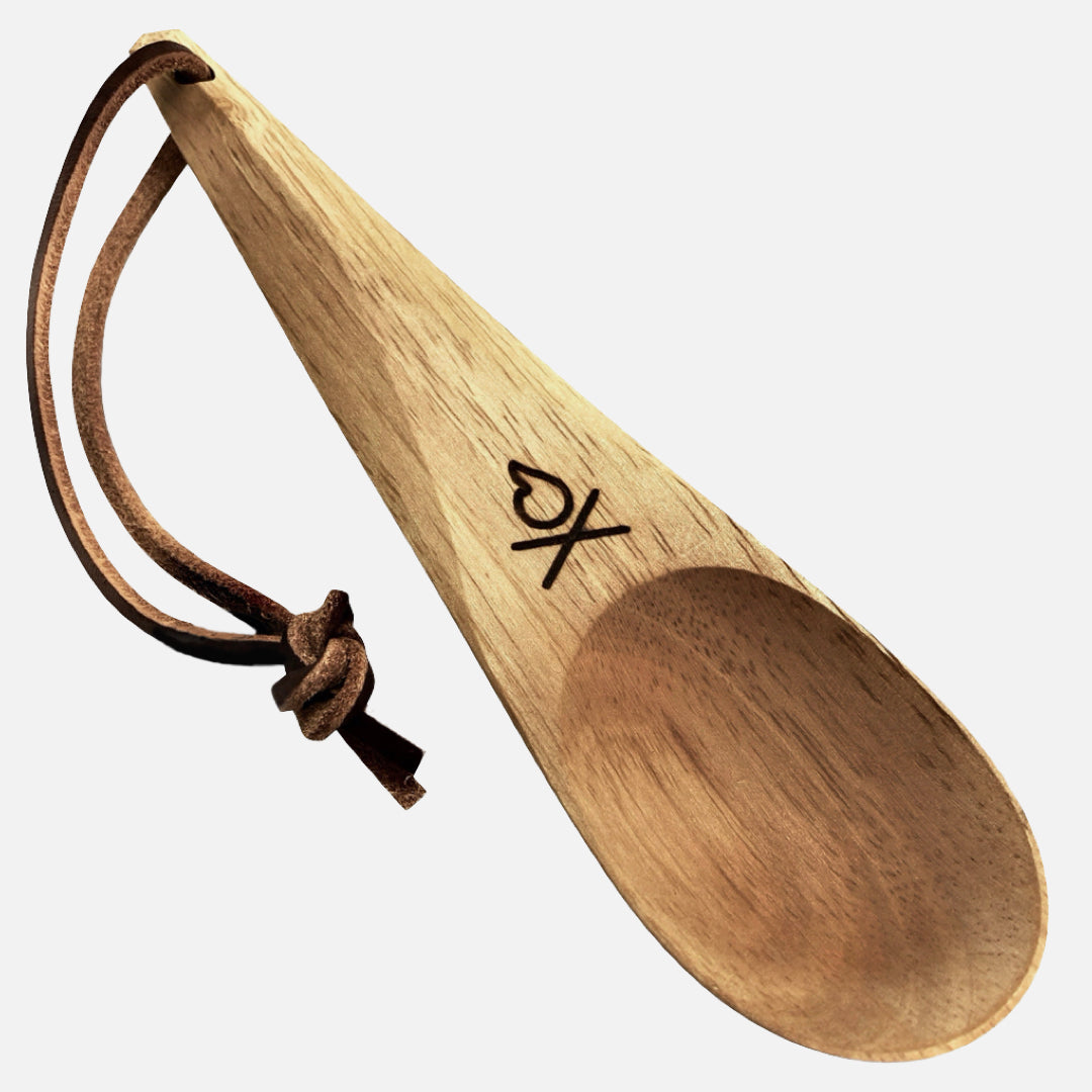 The Überleben Kanu Hardwood Camping Spoon by Überleben features a handcrafted design, leather loop, and engraved heart above an X near the scoop—an eco-friendly kitchen or camping essential shown against a white background.